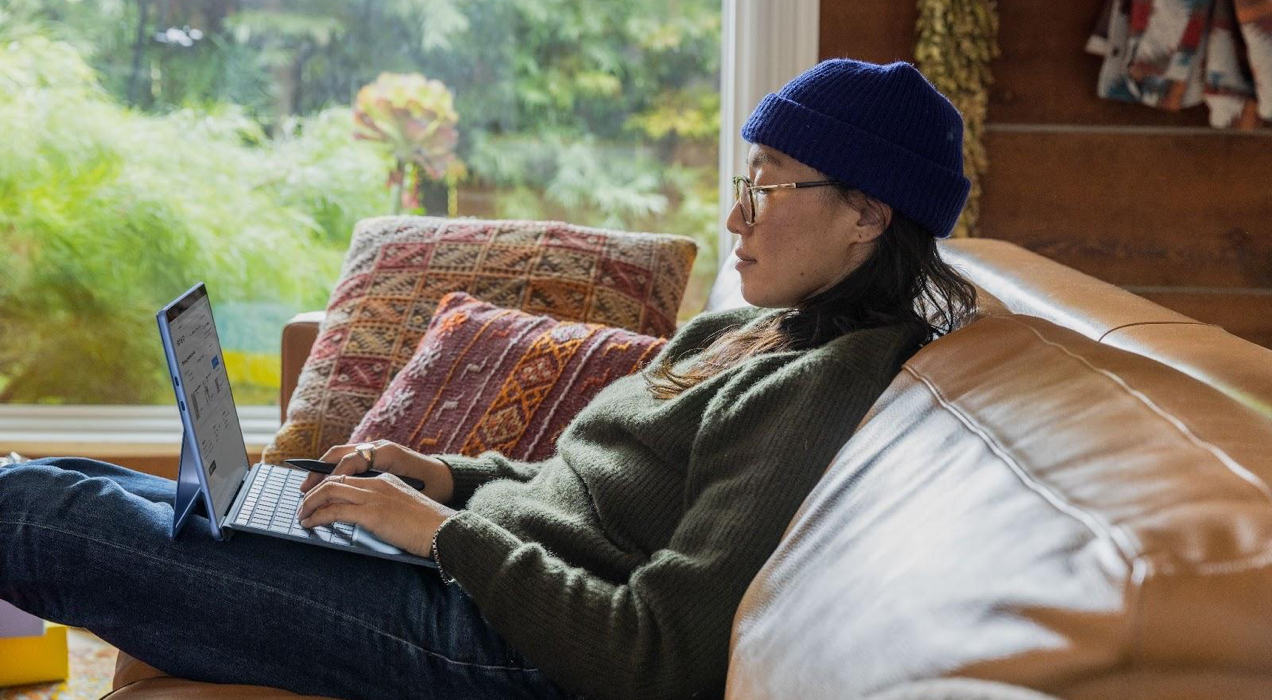 woman wearing a hat, sitting on a couch and looking at a laptop