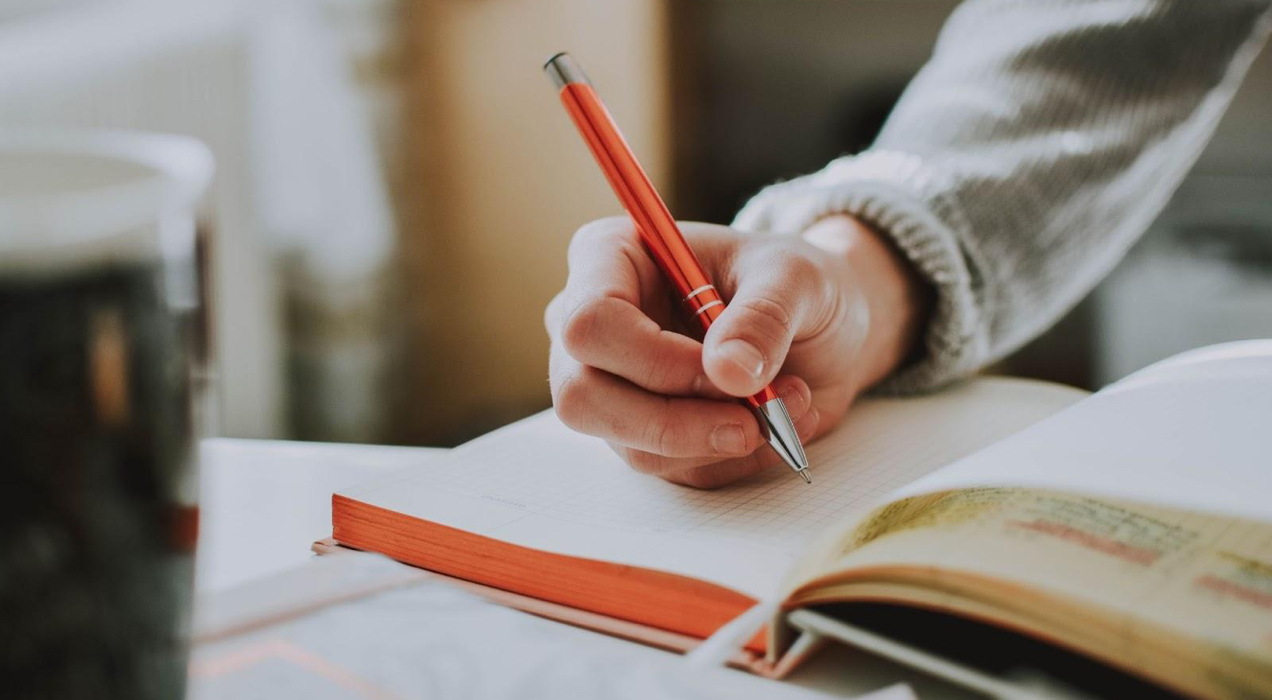 writing in a notebook with an orange pen