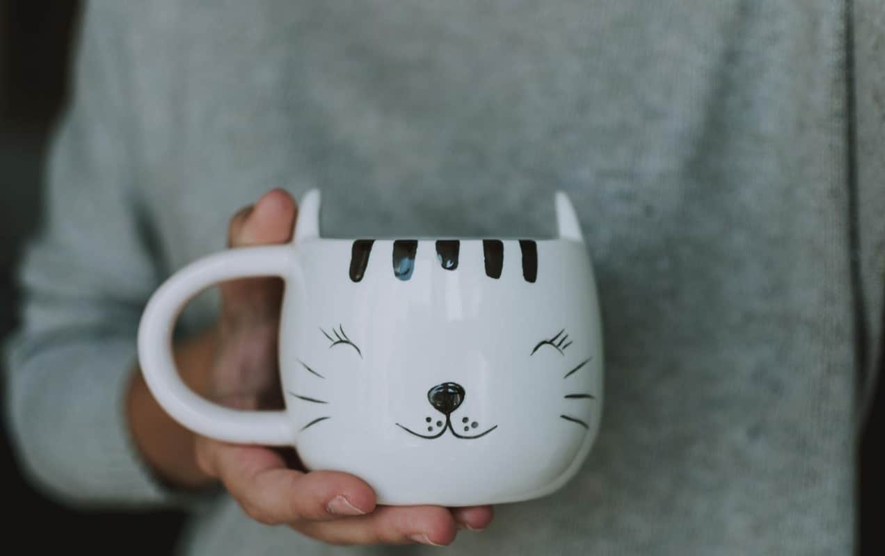 person holding a cat mug in their hand